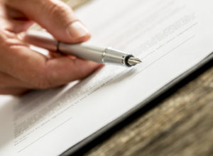 Closeup Of Male Hand Holding An Ink Pen Pointing With Its End On a contract