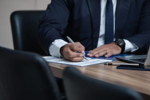 man in business suit signing papers on wooden table